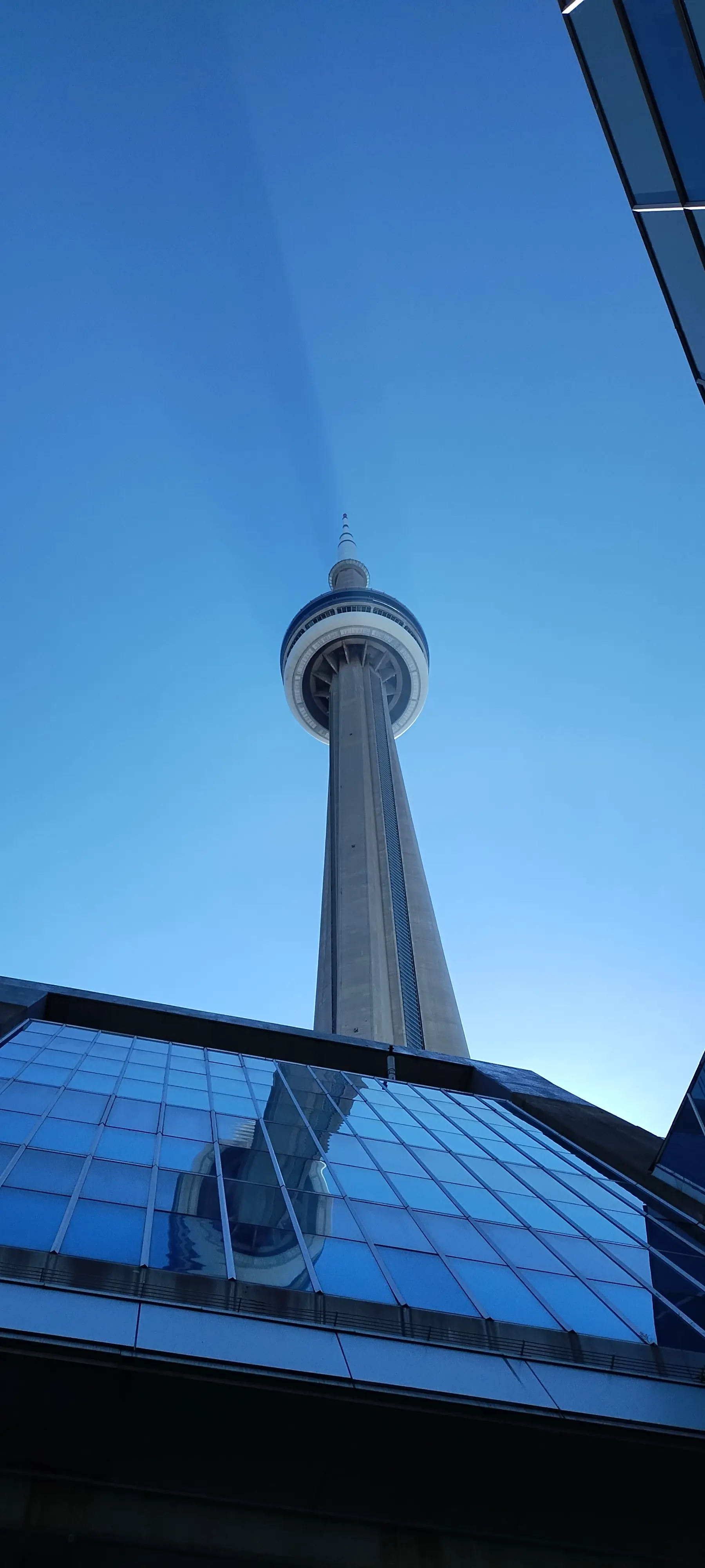 A photo of the CN Tower in Toronto, taken in early morning, where the tower casts a visible volumetric shadow in the air itself